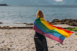 Norsk kvinne med pride-flagg på strand.